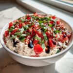 A white bowl filled with creamy bruschetta dip, topped with fresh diced tomatoes, basil, and a balsamic glaze drizzle.