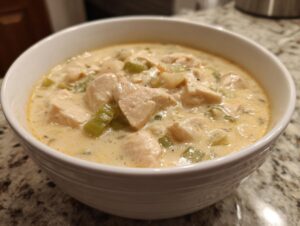 Close-up of a white bowl filled with creamy crockpot white chicken chili, featuring chunks of chicken and celery.