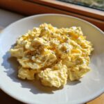 A close-up of creamy, yellow egg salad topped with cracked black pepper served in a white bowl.