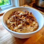 Close-up of a creamy onion dip topped generously with dark, caramelized onions in a white bowl.