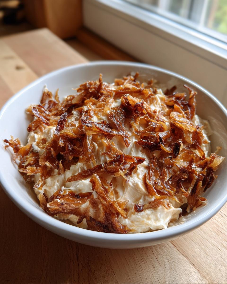 A white bowl filled with creamy onion dip generously topped with crispy, golden brown fried onions.