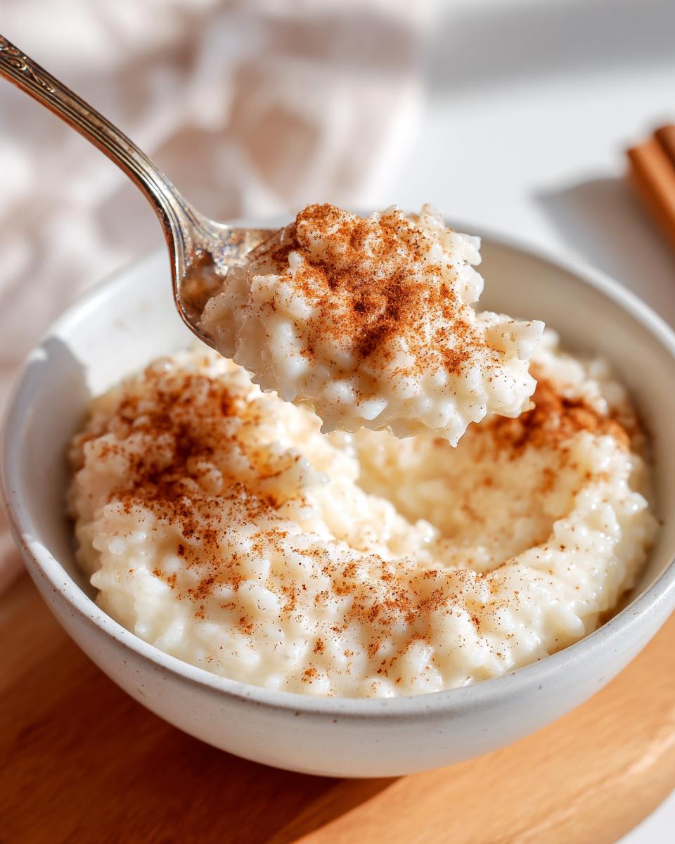 A spoonful of creamy rice pudding recipe topped with cinnamon being lifted from a white bowl.
