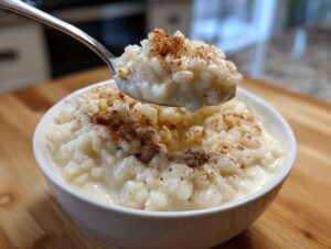 A spoonful of creamy rice pudding recipe topped with cinnamon being lifted from a white bowl.