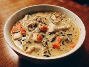 A close-up of a creamy wild rice soup filled with chunks of chicken and bright orange carrots in a white bowl.