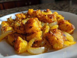Close-up of golden brown, crispy fried potatoes mixed with caramelized onions served on a white plate.
