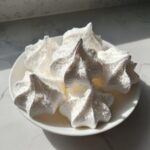 A white plate holding several perfectly piped, star-shaped meringue cookies dusted with coarse sugar.