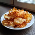 A white plate piled high with homemade, crispy potato chips dusted generously with reddish seasoning.