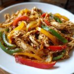 Close-up of shredded chicken mixed with colorful bell peppers and onions, ready for crockpot chicken fajitas.