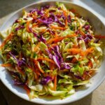 A vibrant bowl of crunchy cabbage salad featuring shredded green cabbage, purple cabbage, and carrots tossed in a light dressing.