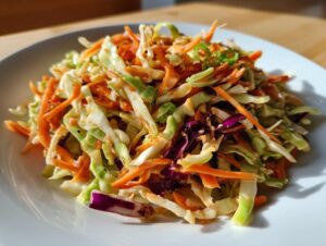 A vibrant mound of crunchy cabbage salad featuring shredded green and purple cabbage mixed with bright orange carrots and a creamy dressing.