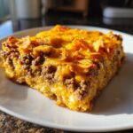 A close-up slice of Dorito Casserole featuring layers of seasoned ground beef, cheese, and a crunchy chip topping.