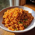 A close-up of fluffy, orange-red spanish rice mixed with green onions and corn served in a white bowl.