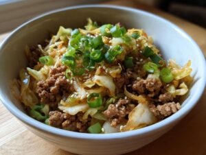 A close-up of a white bowl filled with savory egg roll in a bowl mixture, topped with green onions and sesame seeds.
