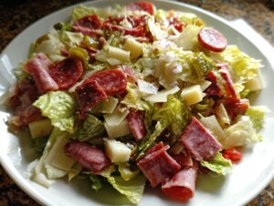 Close-up of a hearty grinder salad featuring chopped lettuce, salami, ham, cheese cubes, and pepperoncini.