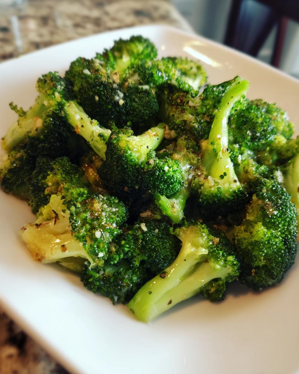 Close-up of vibrant green steamed broccoli florets seasoned with garlic and pepper on a white plate.