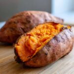 Close-up of a fluffy baked sweet potato split open, revealing bright orange interior.
