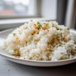 A close-up of fluffy white butter rice garnished with toasted garlic bits and chopped parsley, served on a white plate.