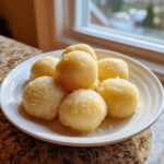 A close-up of several fluffy potato dumplings lightly tossed in butter or breadcrumbs on a white plate.