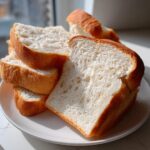 Close-up of several thick slices of fluffy sourdough sandwich bread stacked on a white plate.