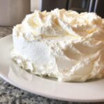 A small cake generously covered in swirls of fluffy, white vanilla buttercream frosting.