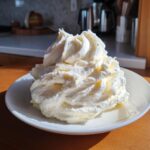 A large, fluffy mound of freshly piped vanilla buttercream frosting sitting on a small white plate.