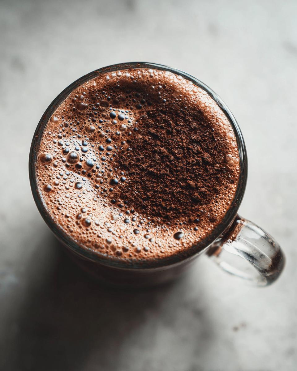 Overhead view of a rich, foamy cup of hot cocoa made from hot cocoa mix, dusted with cocoa powder.