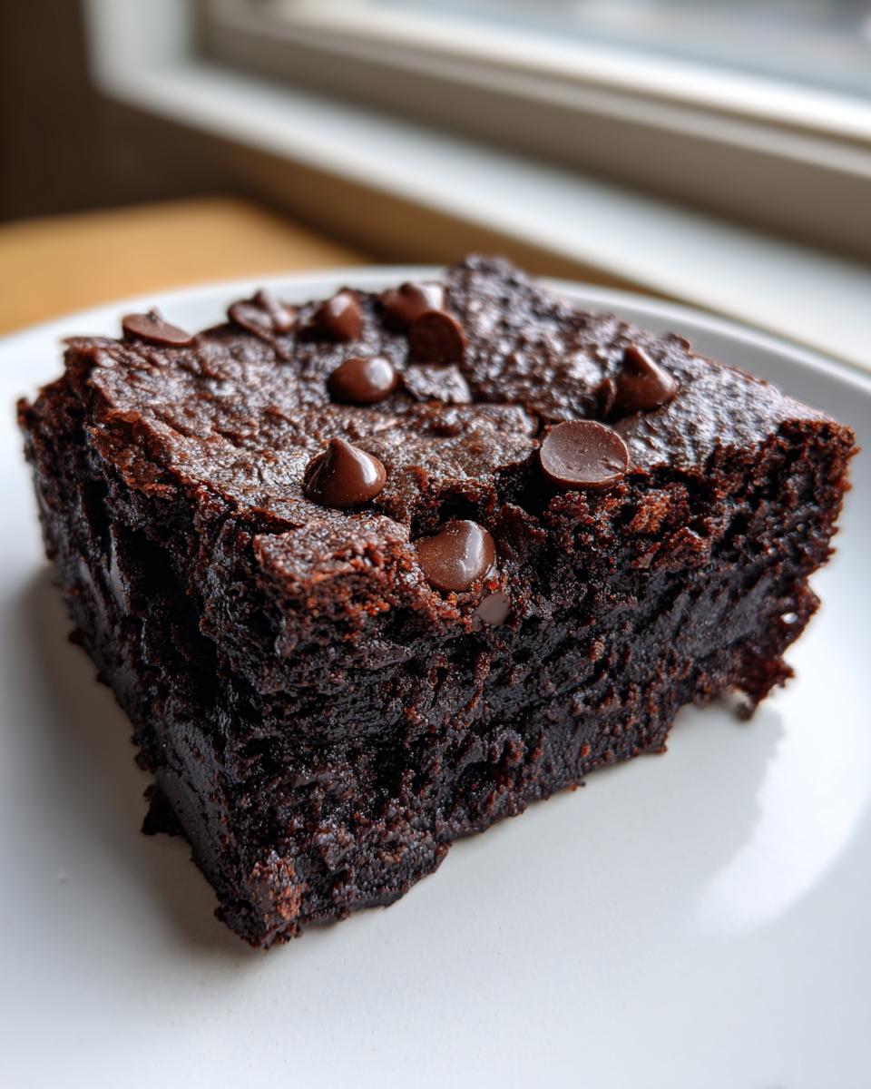 Close-up of a thick, fudgy slice of date brownies topped with melted chocolate chips on a white plate.