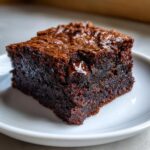 Close-up of a rich, fudgy square of date brownies with a shiny, crackly top and a melted chocolate chip visible.