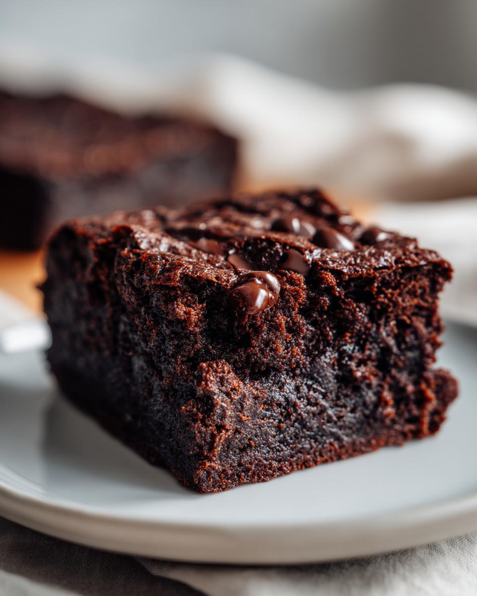 A close-up, fudgy square of dark chocolate sweet potato brownies topped with melted chocolate chips.