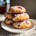 A stack of four delicious cranberry orange cookies topped with a sweet white glaze and dried cranberries.