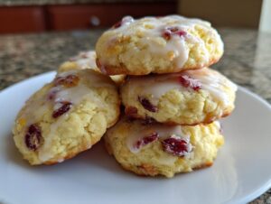 A stack of four soft, glazed cranberry orange cookies piled on a white plate.