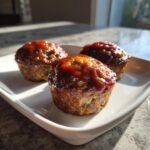 Three perfectly portioned mini meatloaf items topped with a shiny, sweet glaze, resting on a white rectangular dish.