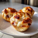 Three golden baked brie bites topped with melted white cheese and dried cranberries served on a white plate.
