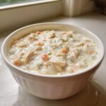 A close-up of thick, creamy homemade cream of chicken soup filled with shredded chicken and diced vegetables in a white bowl.