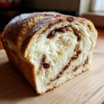 A cross-section of freshly baked raisin bread showing a soft, swirled interior filled with raisins and cinnamon sugar.