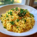 A close-up of bright yellow Mediterranean rice garnished generously with fresh chopped parsley and toasted pine nuts.