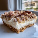 A close-up of a square slice of Million Dollar Pie showing a thick cream layer and a pecan crumb topping.