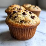 Close-up of a perfectly baked banana chocolate chip muffin topped with melted chocolate chips.