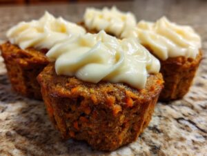 Close-up of several moist carrot cake muffins topped with swirls of cream cheese frosting.
