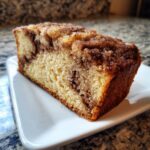 Close-up of a moist slice of cinnamon bread featuring a rich cinnamon swirl and sugary topping.