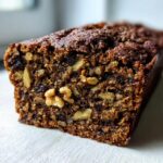 Close-up of a moist slice of dark date nut bread packed with visible walnuts and dried fruit pieces.