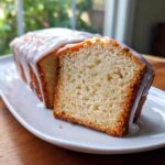 A slice cut from a loaf of moist lemon pound cake topped with a thick, white glaze.