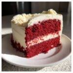 A perfect slice of moist red velvet cake showing two vibrant red layers separated by cream cheese frosting.