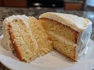 Close-up of a moist slice of vanilla cake recipe, showing the fluffy crumb and thick layer of white frosting.