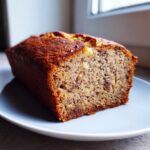 A close-up of a freshly baked slice of vegan banana bread on a light blue plate, showing a moist crumb.