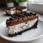 A perfect slice of no bake Oreo pie showing a dark crust, white cream layer, chocolate mousse top, and cookie crumbles.