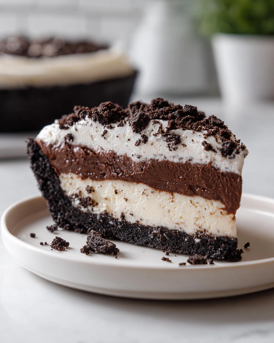A perfect slice of no bake Oreo pie showing a dark crust, white filling, chocolate layer, and whipped topping with cookie crumbles.