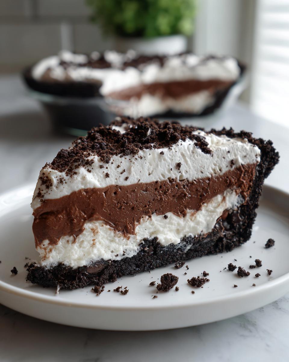 A delicious slice of no bake Oreo pie showing layers of dark crust, white cream, chocolate mousse, and whipped topping.