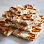 A stack of broken pieces of white chocolate peanut butter pretzel bark topped with mini pretzels and sea salt.