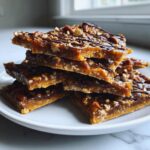 Close-up of stacked, broken pieces of homemade Pecan Pie Bark topped with pecans and drizzled chocolate.